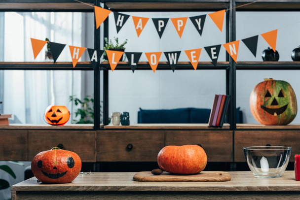 close up view of pumpkins on wooden tabletop and hanging flags with happy halloween inscription in empty room - Photo, Image