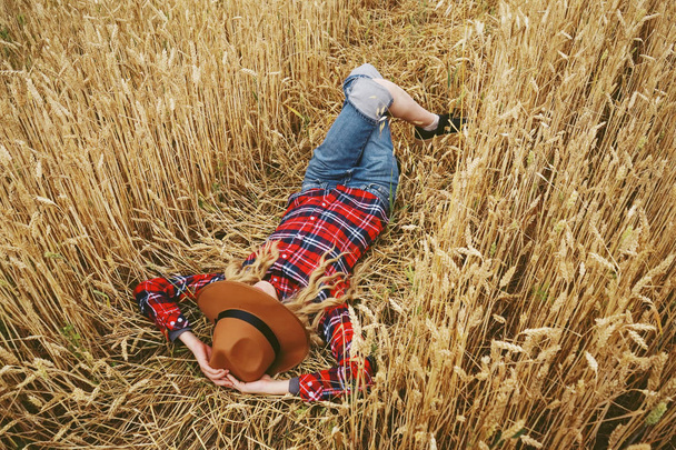 カントリー スタイルを持つ若い女性は小麦畑で休憩します。  - 写真・画像