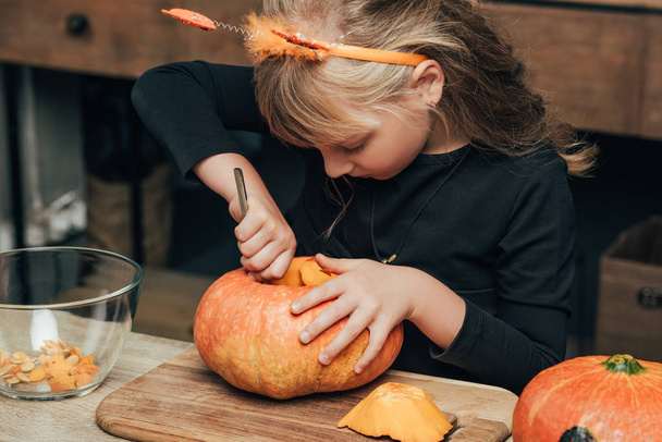 cute kid carving pumpkin for halloween alone at tabletop at home - Photo, Image