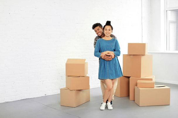 Feliz pareja interracial con cajas de cartón en la habitación. Mudándose a casa nueva
 - Foto, imagen