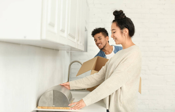 Happy interracial couple unpacking box in kitchen. Moving into new house - Φωτογραφία, εικόνα
