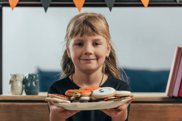 Portret van een glimlachend kind weergegeven: plaat met halloween cookies thuis - Foto, afbeelding