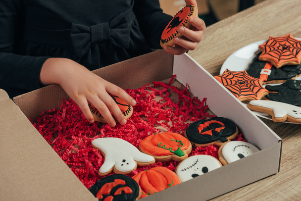 vista parziale del bambino che organizza biscotti di Halloween a tema sul tavolo di legno a casa
 - Foto, immagini