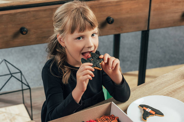 roztomilé dítě jíst halloween cookie a při pohledu na fotoaparát doma - Fotografie, Obrázek