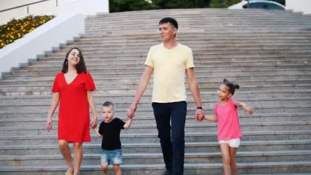 Young happy family: father, mother, daughter and son in the Park. They go down the stairs and talk. - Footage, Video