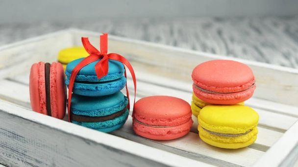 красивые вкусные кондитерские печенья макароны разноцветные макароны на деревянном фоне в виде подарка с красным бантом
 - Фото, изображение