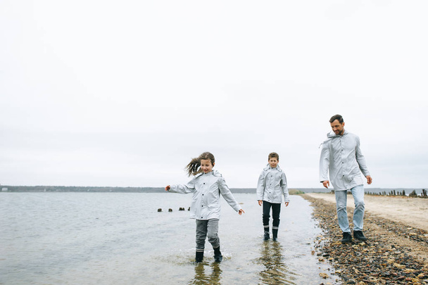 Beautiful family portrait dressed in raincoatnear the sea - Fotoğraf, Görsel