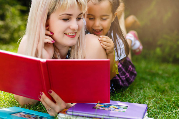 Bonita jovem mãe lendo livro para sua filha no prado verde
 - Foto, Imagem