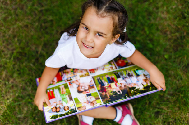 Portré a kis aranyos lány nyári zöld park ül könyvével, felülnézet - Fotó, kép