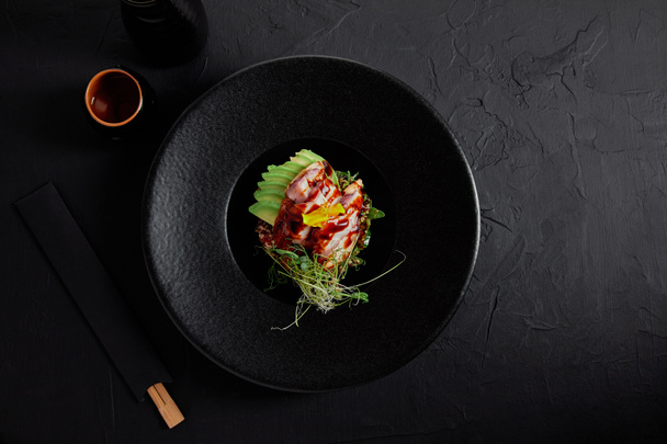 felülnézet ízletes hagyományos japán étel, a tenger gyümölcsei-, avokádó- és gyógynövények a fekete lemez - Fotó, kép