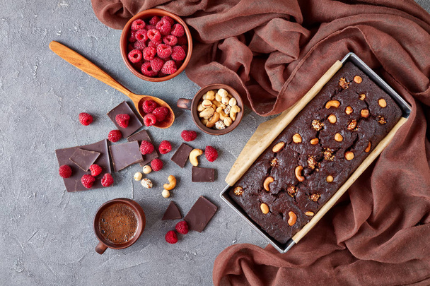 delicious chocolate pound cake from gluten free buckwheat flour with nuts and raspberries in a metal baking mold on a concrete table with cup of coffee, view from above, flat lay, close-up - Zdjęcie, obraz