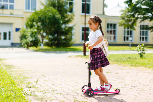 Pequena criança aprendendo a andar de scooter em um parque da cidade no dia ensolarado de verão. Bonita menina montando um rolo. Lazer ativo e esporte ao ar livre para crianças
. - Foto, Imagem