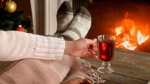 Closeup image of woman in woolen socks lying by the fireplace and drinking hot tea - Photo, Image