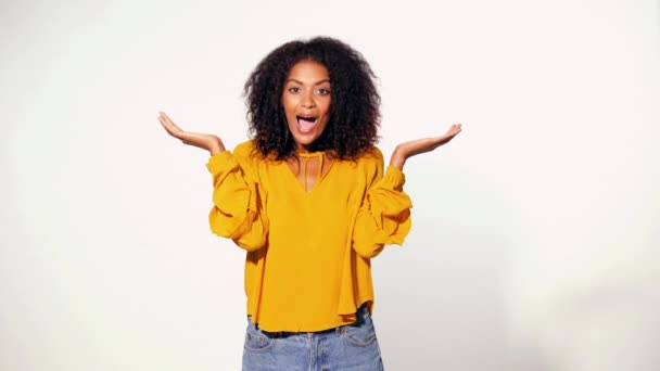 Pretty african woman in yellow wear learned pleasant news and is happy with what was heard over white background. Cute mixed race girl shocked, saying WOW. - Séquence, vidéo