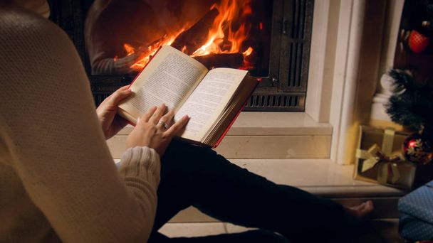 Closeup image of young woman sitting by the fireplace and reading book - Photo, image