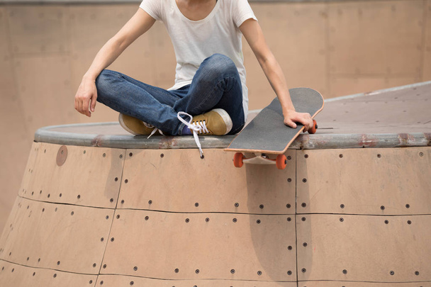 Woman skateboarder sitting on skatepark ramp  - Photo, image