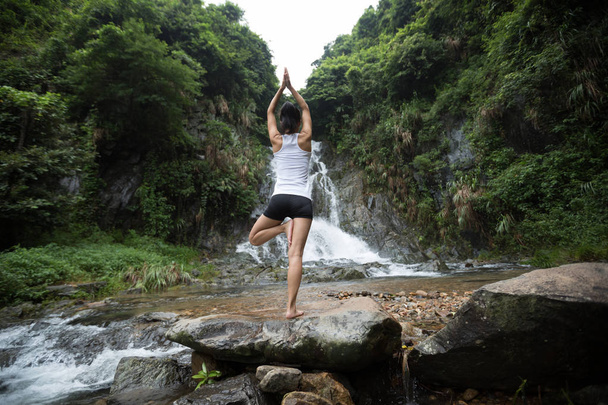 Young woman practicing yoga near waterfall in forest - Foto, Bild