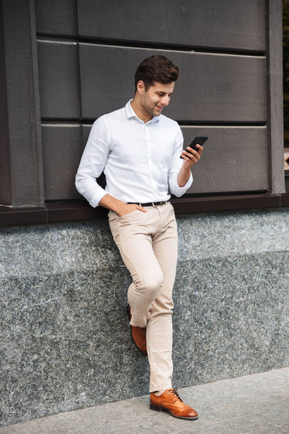 Attraente giovane manager maschio formale vestito appoggiato a un muro all'aperto, utilizzando il telefono cellulare
 - Foto, immagini