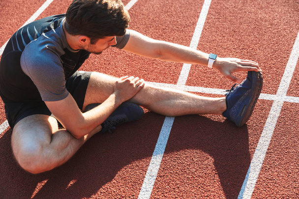 Knappe sportman doen stretching oefeningen in het stadion - Foto, afbeelding