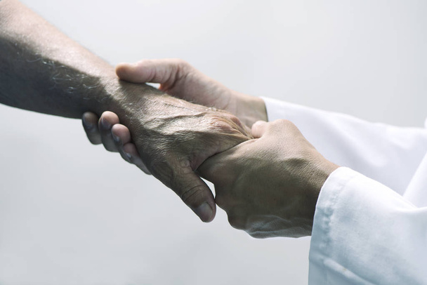 Nahaufnahme eines kaukasischen Mannes im weißen Mantel, der die Hand eines älteren kaukasischen Patienten bewegt - Foto, Bild