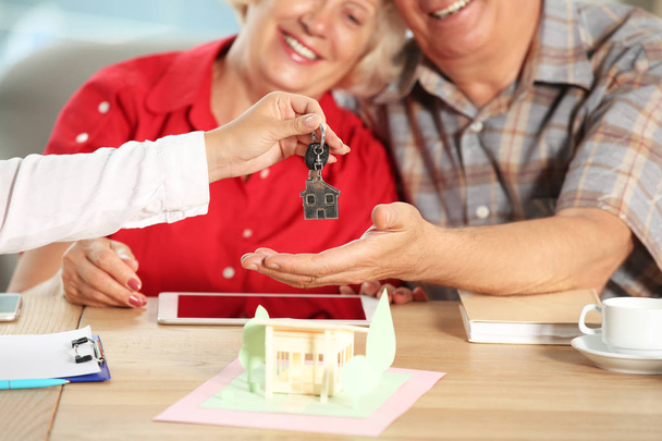 Agente imobiliário dando chave de casa nova para casal maduro feliz no escritório
 - Foto, Imagem
