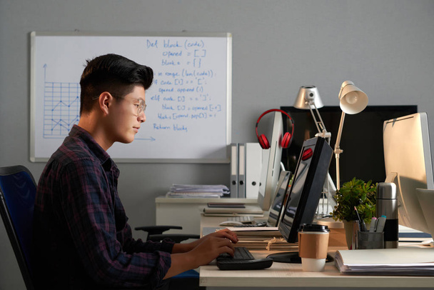 Азіатський програміст, сидячи перед комп'ютером і працює - Фото, зображення