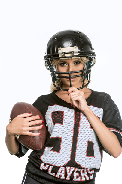 jovem mulher séria em uniforme de futebol americano com bola olhando para a câmera isolada no branco
 - Foto, Imagem