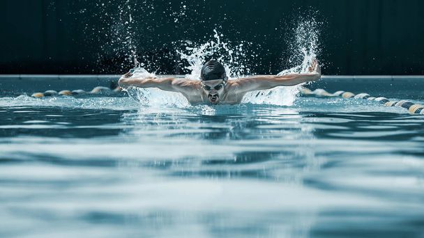 dynamic and fit swimmer in cap breathing performing the butterfly stroke - Fotografie, Obrázek