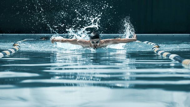 dynamic and fit swimmer in cap breathing performing the butterfly stroke - Фото, изображение
