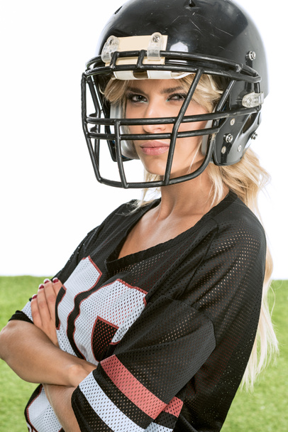 grave jovem mulher no americano futebol uniforme olhando para a câmera com os braços cruzados isolado no branco
 - Foto, Imagem