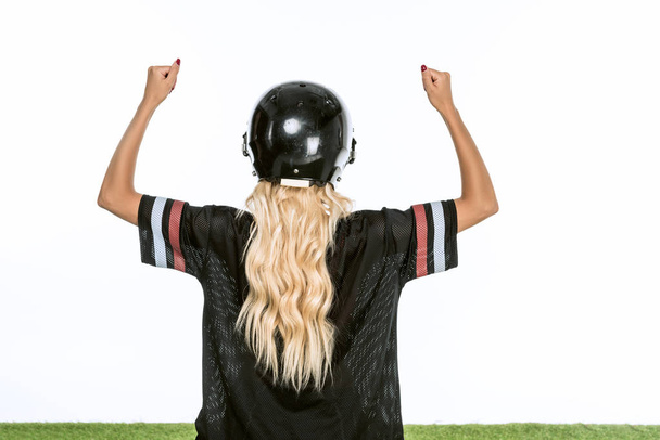Rückansicht einer Frau in American-Football-Uniform, die den Sieg feiert, während sie isoliert auf weißem Rasen steht - Foto, Bild