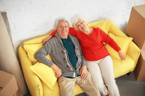 Ώριμο ζευγάρι που κάθεται στον καναπέ κοντά σε κουτιά Αφού μετακόμισε σε νέο σπίτι - Φωτογραφία, εικόνα