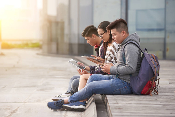 Grupo de estudiantes asiáticos sentados al aire libre y navegando por Internet en tabletas digitales modernas
 - Foto, Imagen