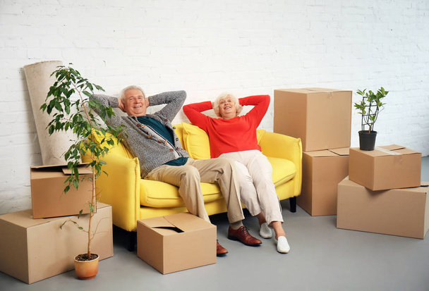 Älteres Paar sitzt nach Einzug in neues Haus auf Sofa neben Kisten - Foto, Bild