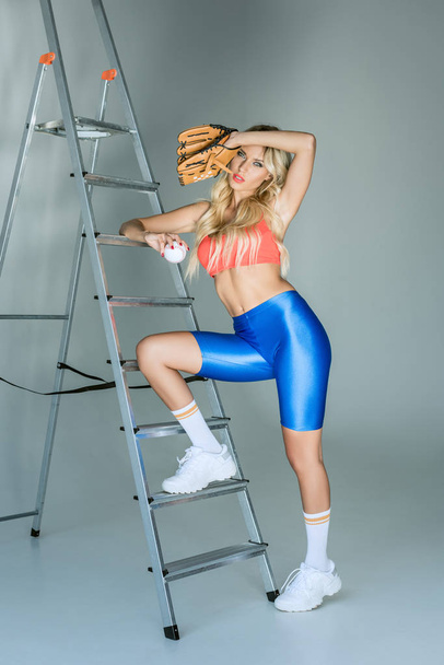 sporty young woman standing on stepladder with baseball glove and ball - Φωτογραφία, εικόνα