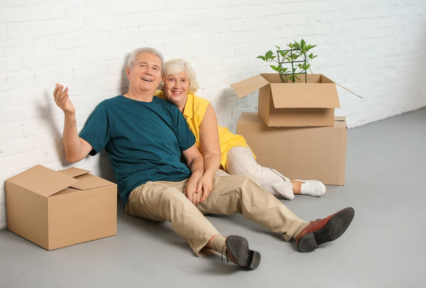 Heureux couple mature avec des boîtes assises sur le sol dans leur nouvelle maison
 - Photo, image