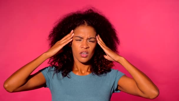 Frustratated african american woman with curly hair in green t-shirt with headache over pink wall background. Girl is tired of work, she has depression, illness. - Záběry, video