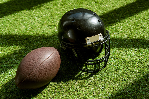 yeşil çimenlerin üzerinde Amerikan futbolu topu ve kask yüksek açılı görünüş - Fotoğraf, Görsel