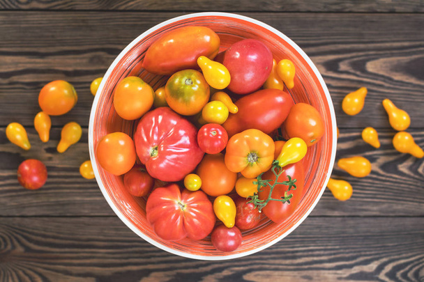 viele verschiedene rote orange gelbe Tomaten auf dunkler Holzoberfläche. schöne Lebensmittel Kunst Hintergrund, Ansicht von oben. - Foto, Bild