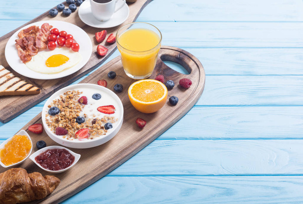 Reggeli: a joghurt, tojás, bogyós gyümölcsök, gyümölcslé, croissant és jam - Fotó, kép