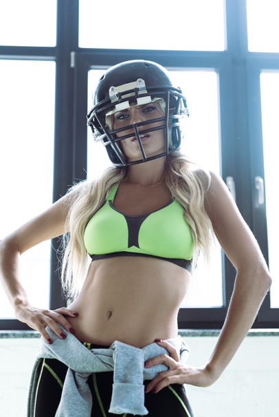 urheilullinen nuori nainen urheilussa rintaliivit ja amerikkalainen jalkapallo kypärä katselee kameraa
 - Valokuva, kuva
