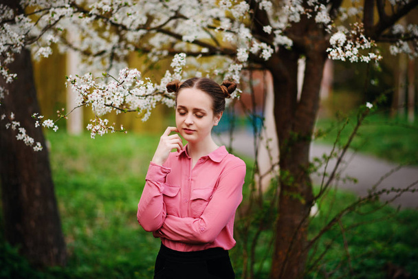 Krásná mladá dívka v růžové košili, stojící pod kvetoucí jabloň a užívat si slunného dne. Rozkvetlé jaro - Fotografie, Obrázek