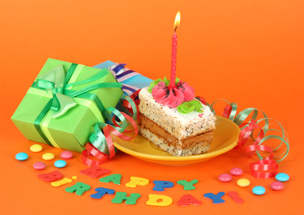 Colorful birthday cake with candle and gifts on orange background - Фото, изображение