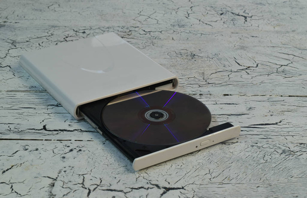 External CD/DVD/Blu-Ray Drive with opened tray and golden Blu-ray (BD) disc on white wooden background (left angle view) - Photo, Image