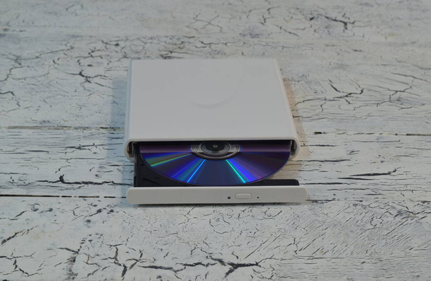 CD / DVD / Blu-Ray Drive esterno con vassoio aperto e disco Blu-ray (BD) viola su sfondo bianco in legno (vista angolare frontale)
) - Foto, immagini