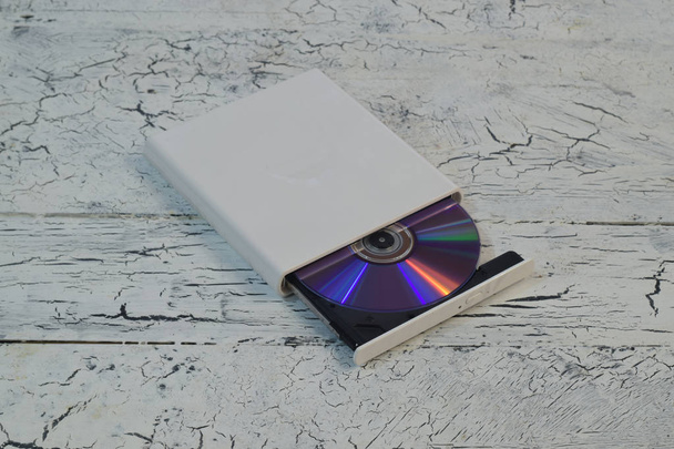 External CD/DVD/Blu-Ray Drive with opened tray and purple Blu-ray (BD) disc on white wooden background (left angle view) - Photo, Image