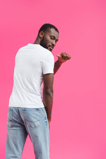 vista posterior del hombre afroamericano apuntando a la camisa blanca en blanco aislada en rosa
  - Foto, imagen