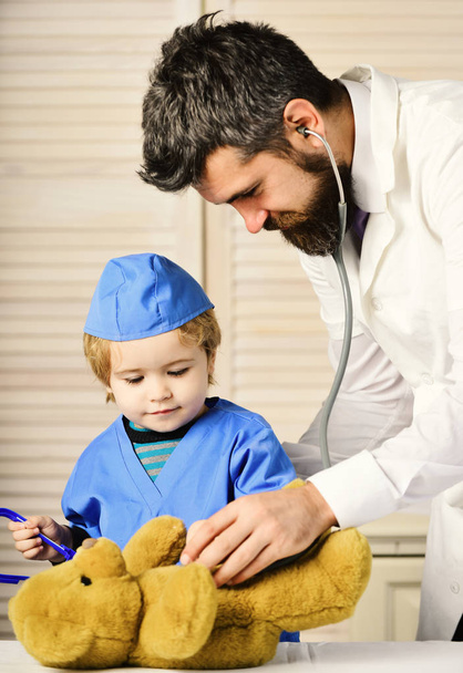 Mann mit Bart und Junge halten Stethoskop auf Holzboden. - Foto, Bild