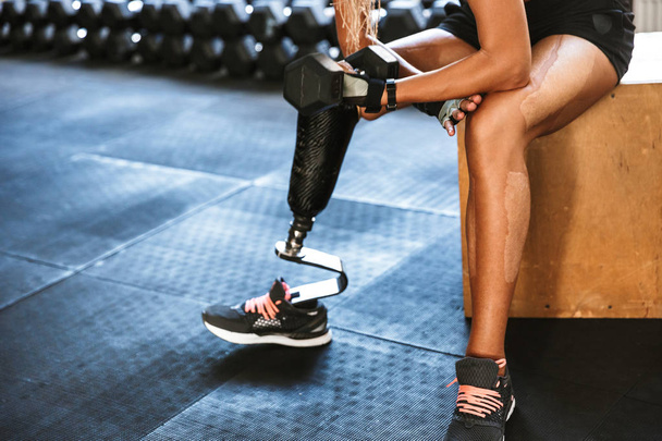 Cropped image of fitness disabled invalid woman wearing prosthesis in tracksuit training and lifting dumbbell in gym - Foto, Bild