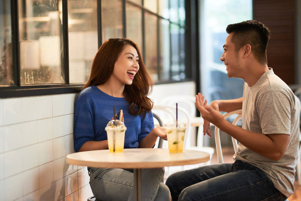 Asiatico giovane coppia agghiacciante in caffè avendo bevande in tazze e ridere felicemente mentre chatta
 - Foto, immagini